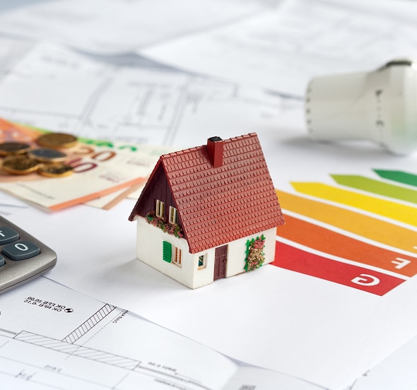 Coût Énergie Maison : Calcul et Performance Maison miniature posée sur des documents financiers et un certificat de performance énergétique (lettre E visible) avec de l'argent (billets de 20€) et un calculateur.